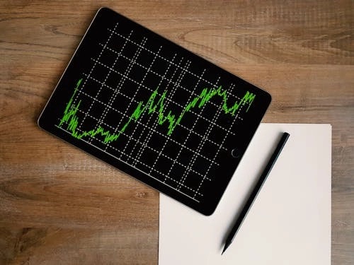 Tablet displaying a rising financial chart beside a notebook and pen on a wooden desk