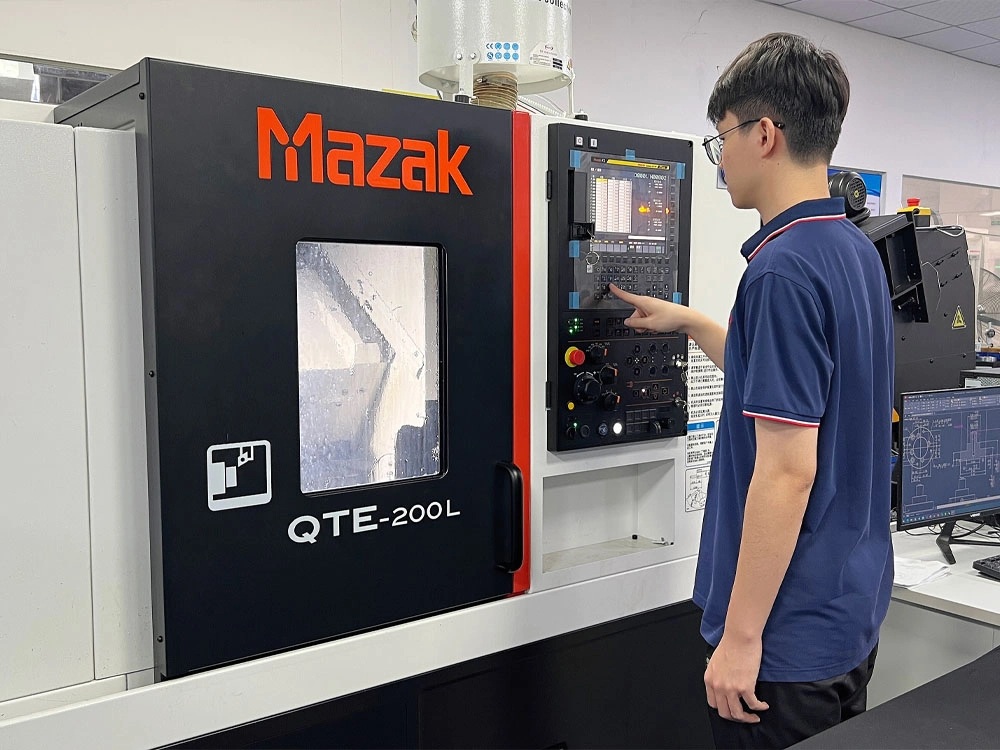 Technician operating a Mazak CNC lathe using the machine’s control panel in a workshop