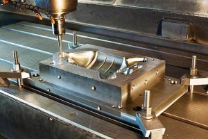 The image shows a CNC machine precisely milling a metal mold fixed on a worktable